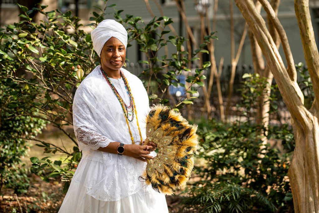 kameelah martin dressed in white holding an ornate feather fan