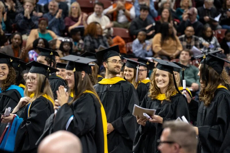 Graduates standing and dressed in graduation cap and gowns.