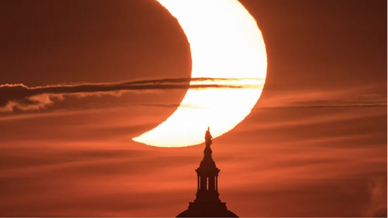 partial solar eclipse with red sky and church steeple
