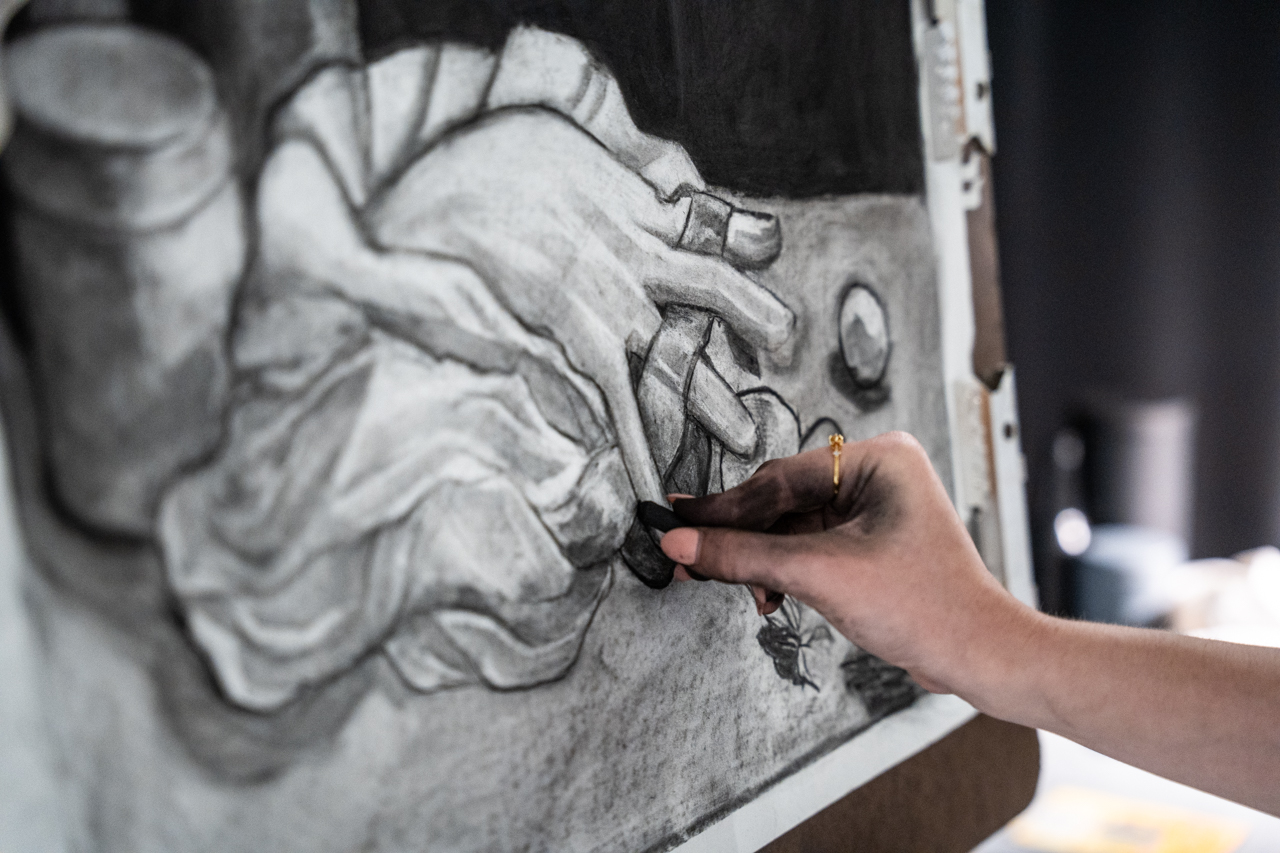 close up of a student using charcoal to draw a hand 