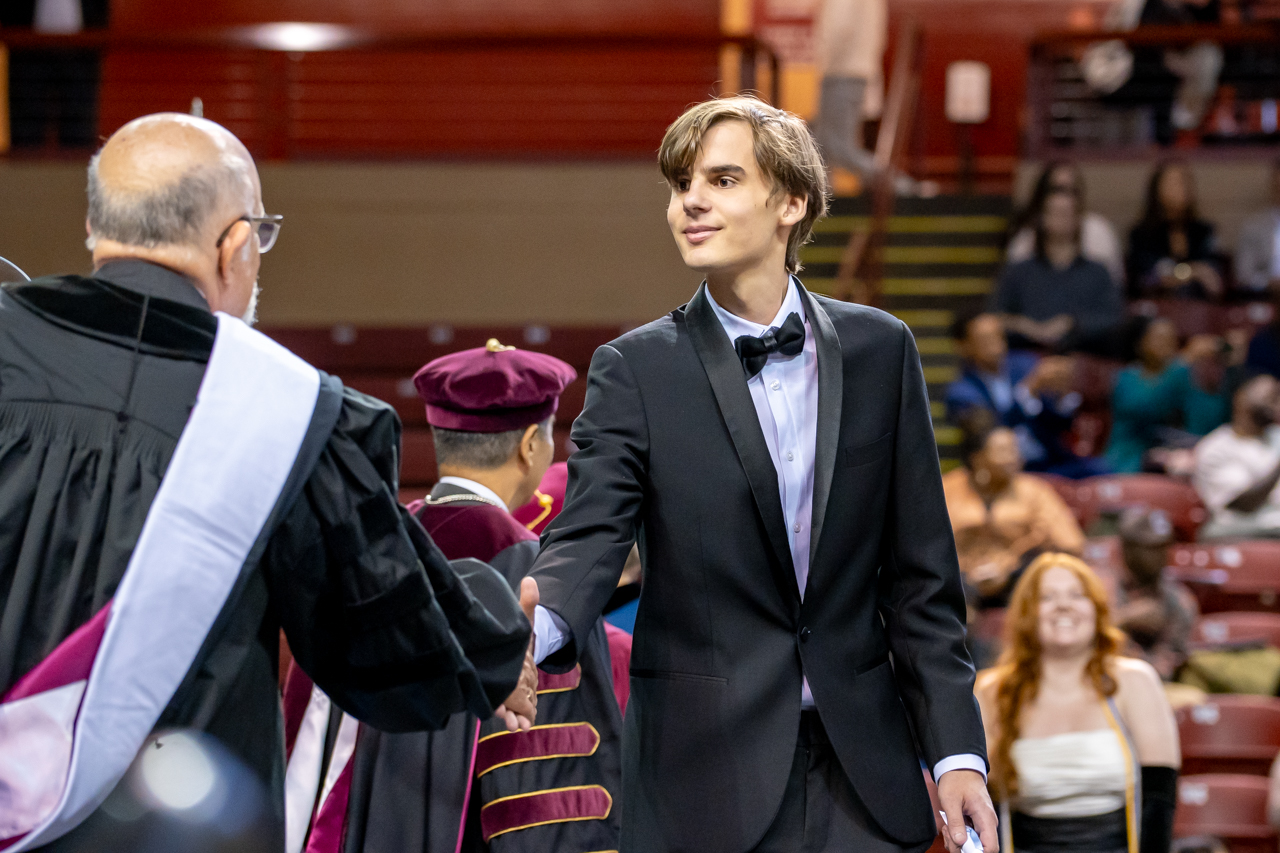 students walk across to receive their diploma