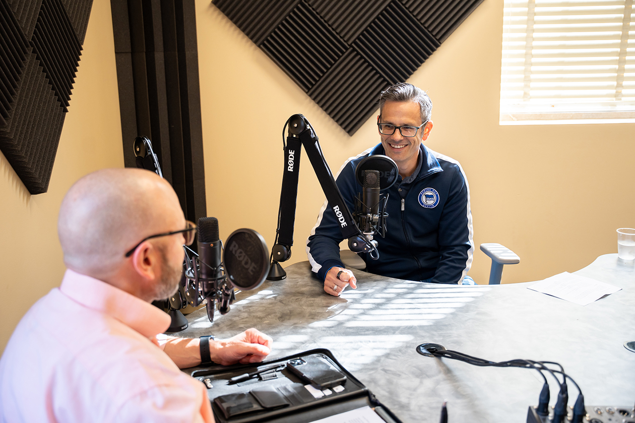 Chris Korey laughs in front of podcast microphone