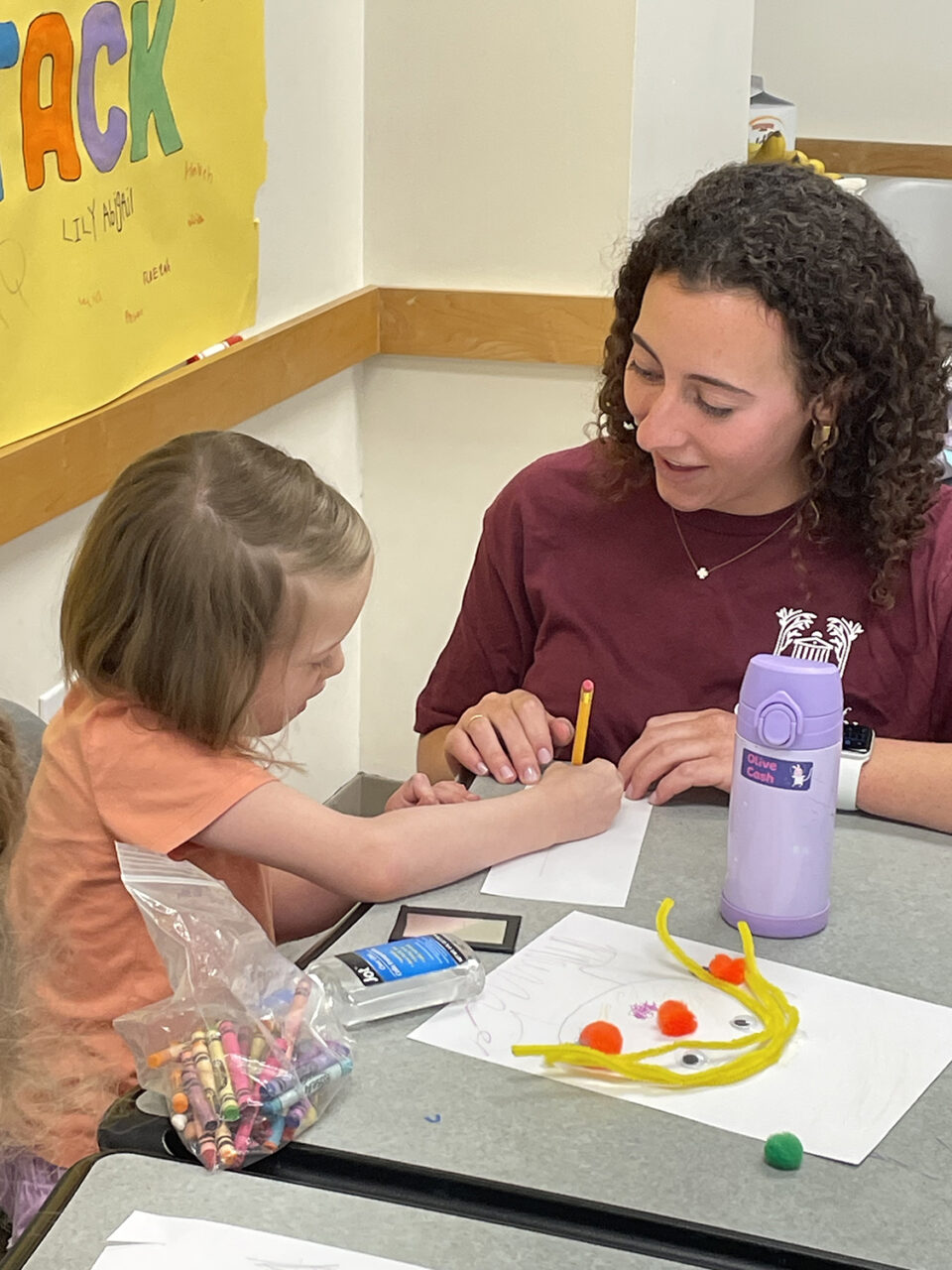 college student helps a child with an art project