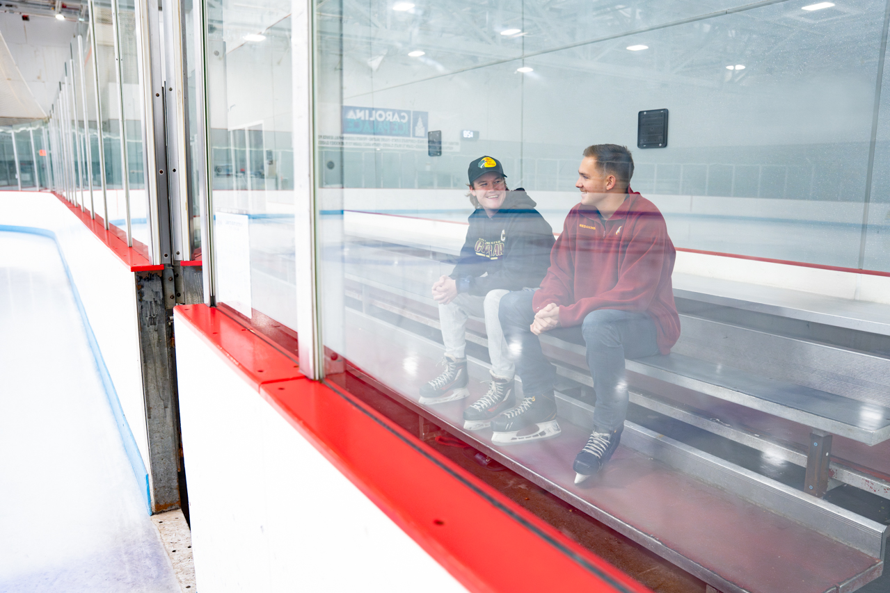 two guys sitting on a bench outside the rink talking
