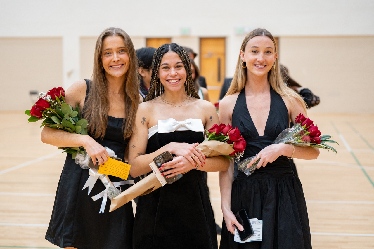three graduate girls hold flowers 