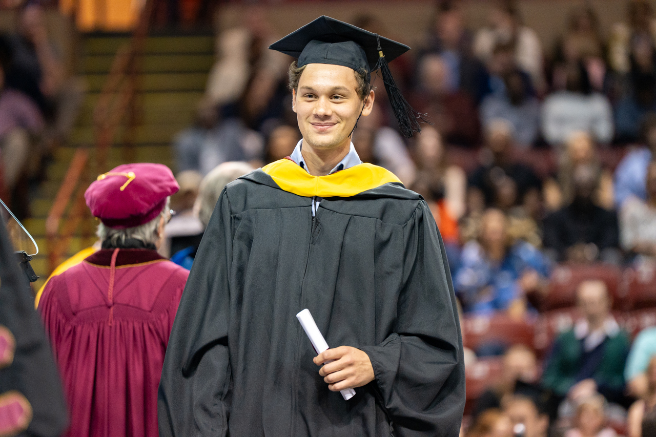 male student walks across the stage with a diploma in hand