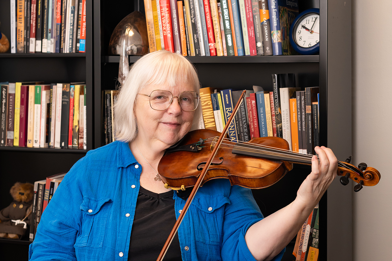woman plays violin in front of bookcase