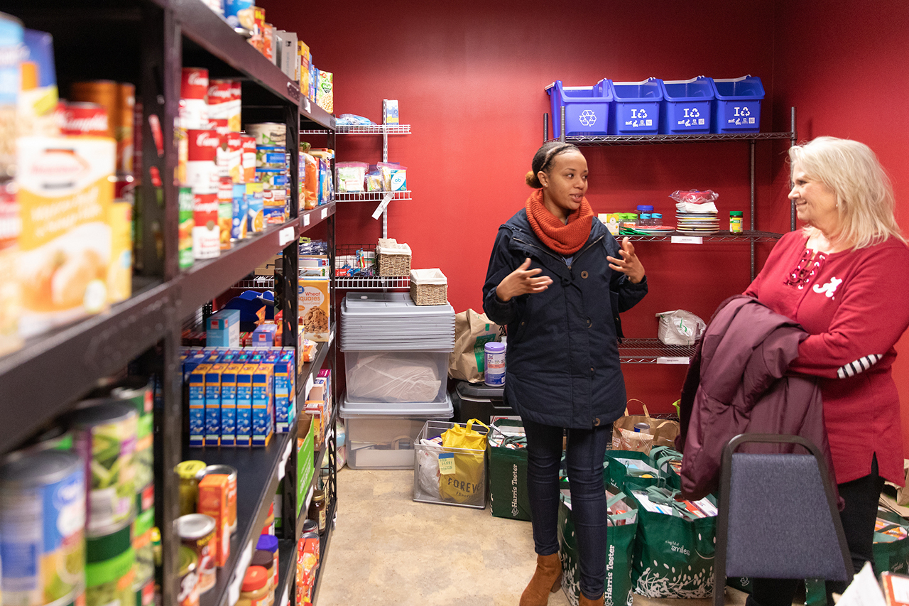 two women talk inside a pantry full of canned goods