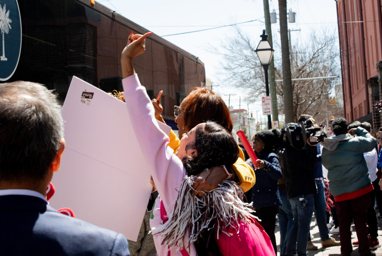 two women hug and wave at bus