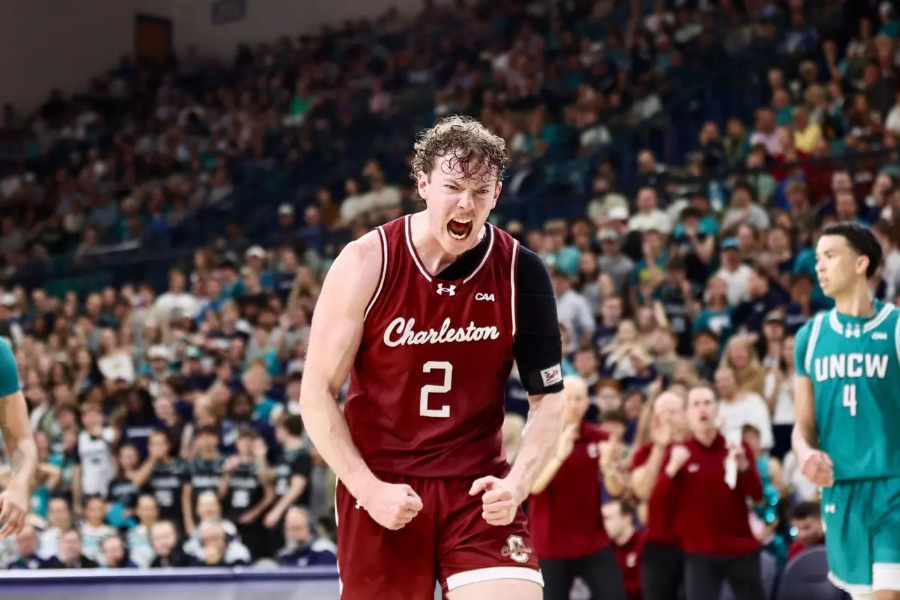 A basketball player in a maroon Charleston jersey, number 2, clenches his fists and shouts in celebration on the court, with teammates and a cheering crowd in the background.