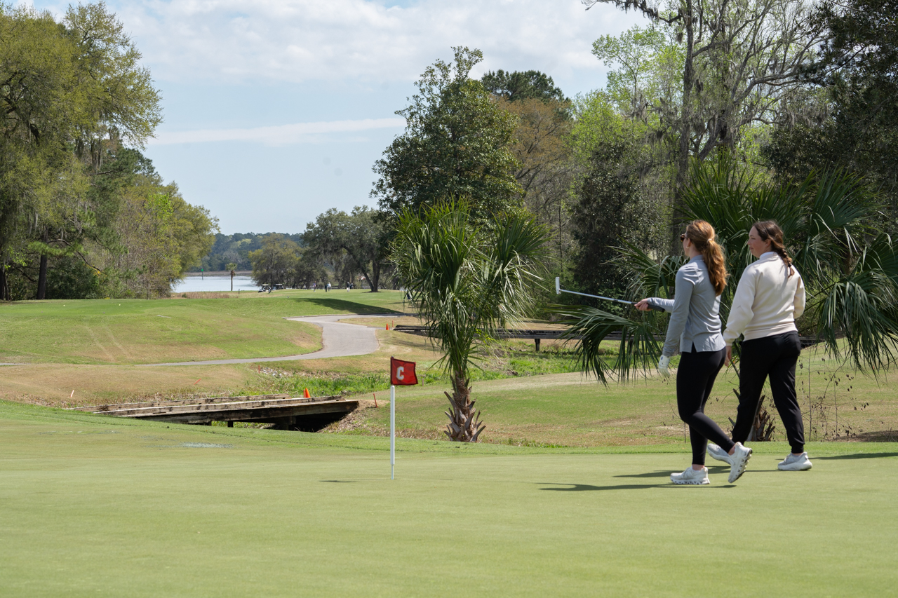 walking to hole with view of golf course behind them