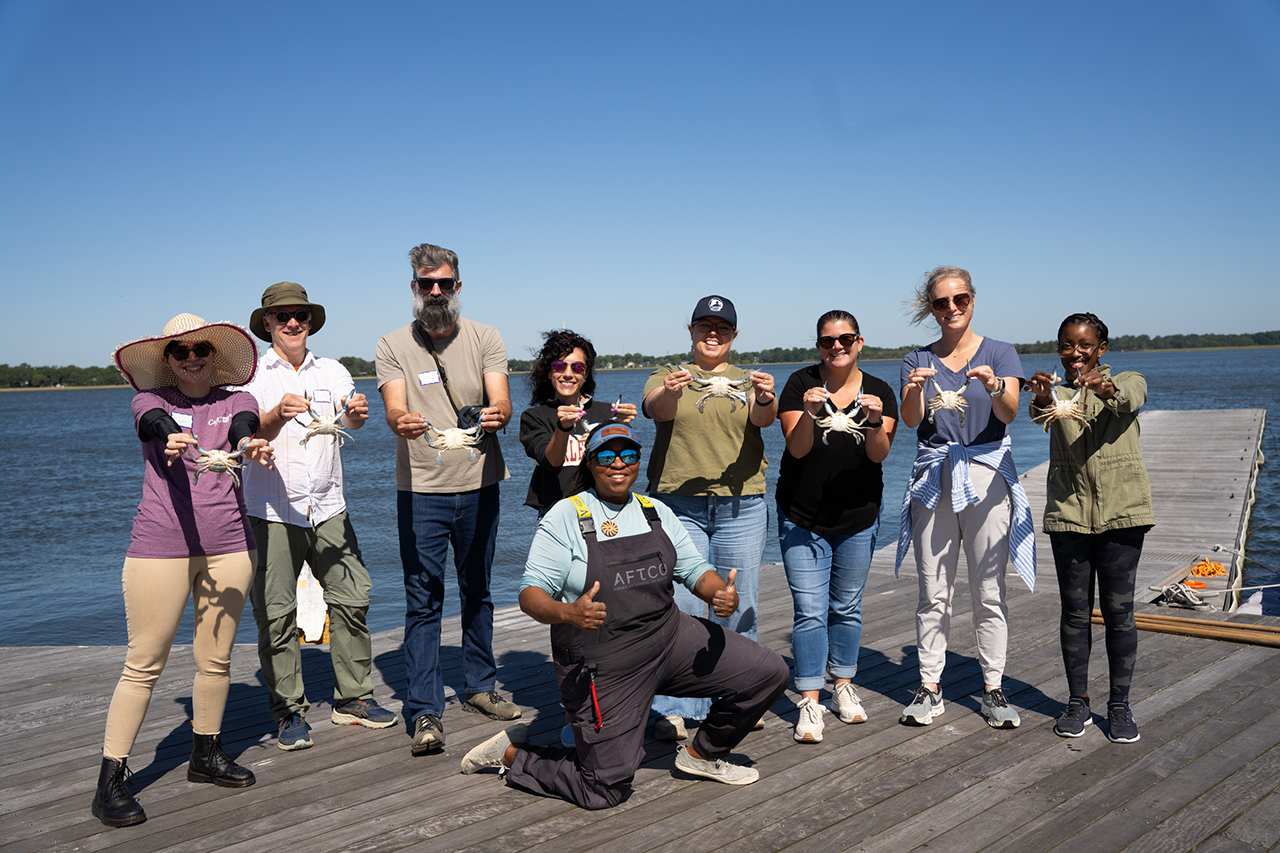 A group of people on a wooden dock by the water, each holding a crab and smiling for the camera.
