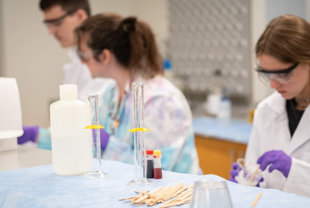 lab items are in focus on counter while students are soft in the background working on experiments in the lab