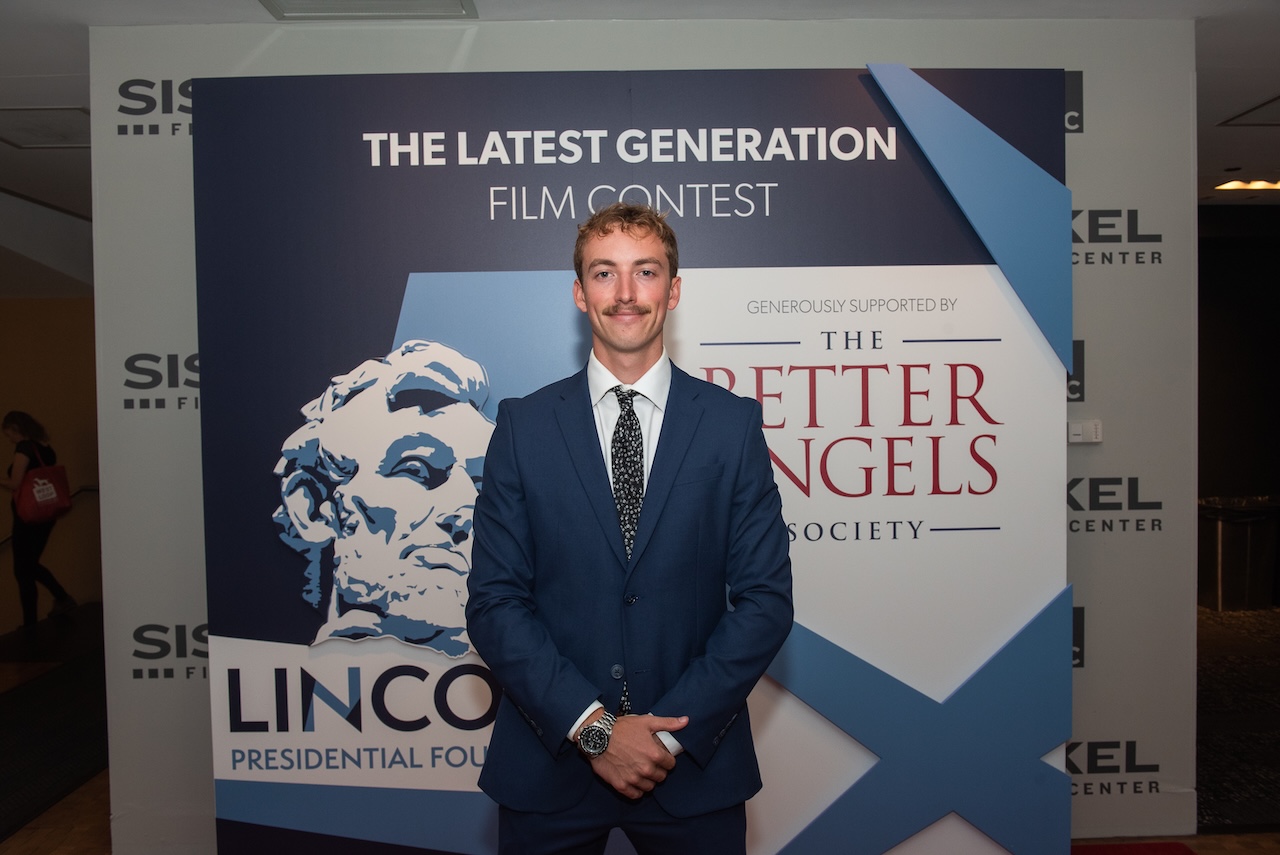 College of Charleston student Jakob Highducheck standing in front of a sign at the Latest Generation Film Contest