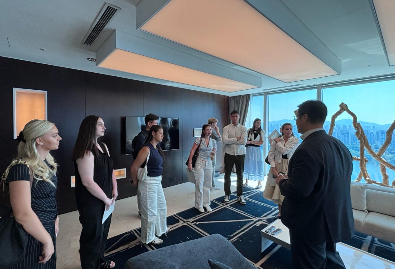 Hospitality major students standing in a group in a hotel in South Korea learning from a professional in the hospitality industry.