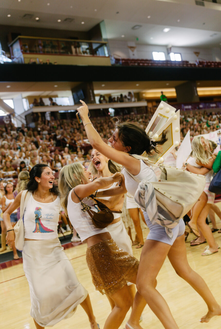 A group of young people celebrate energetically on a basketball court, surrounded by a large crowd in the stands.