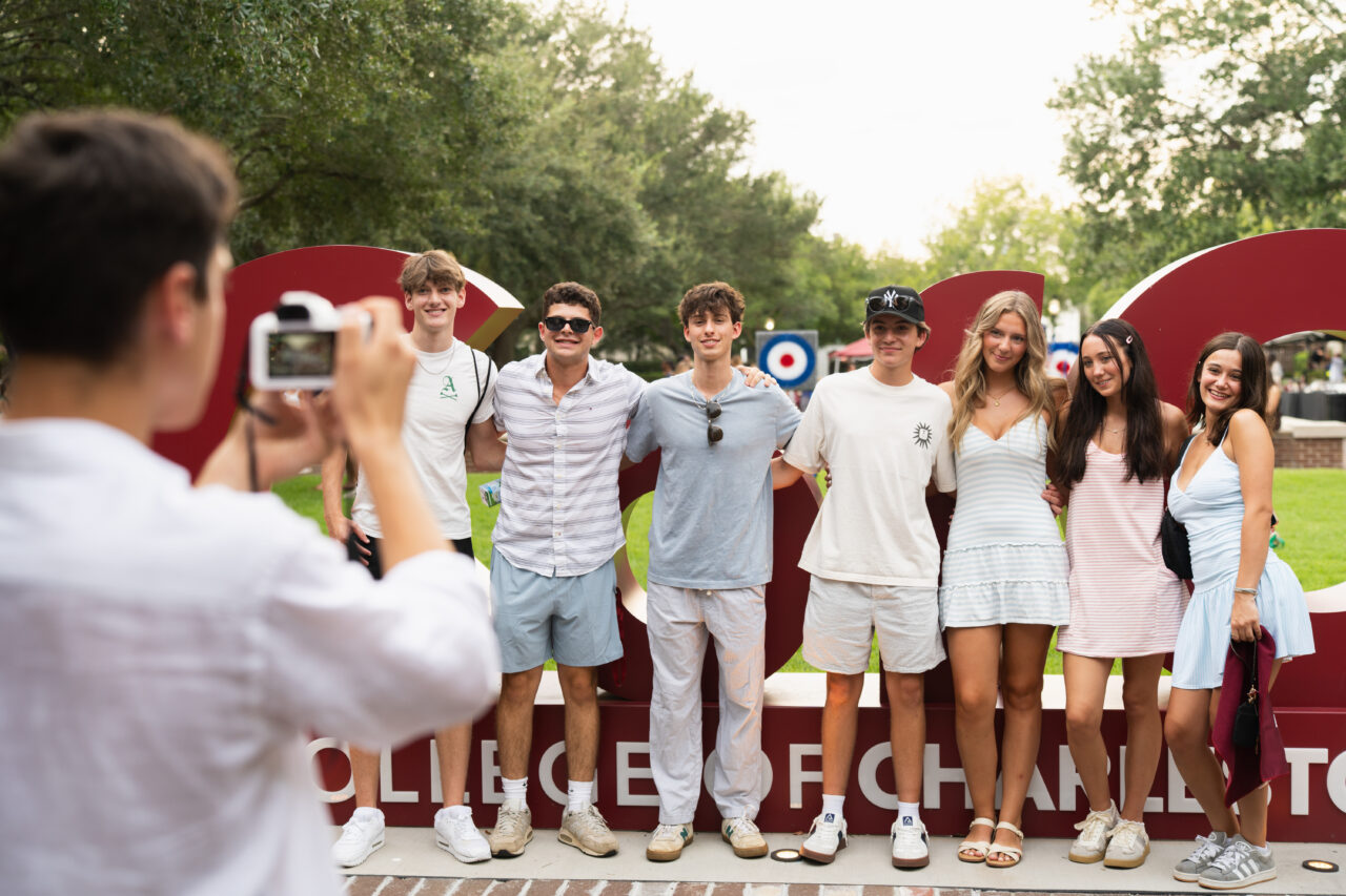 A group of young people pose together for a photo outdoors, with one person capturing the moment using a camera.