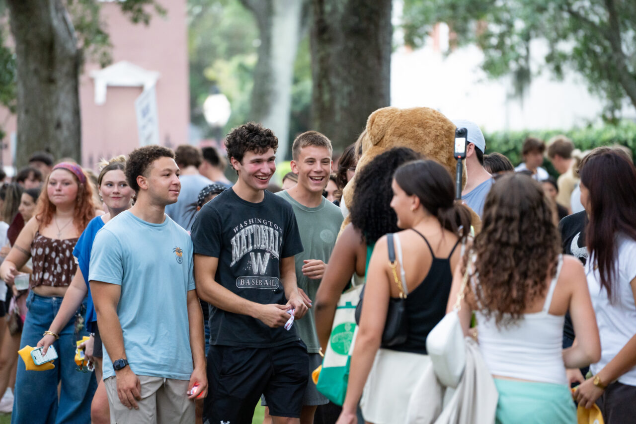 A group of young people gather outdoors, smiling and interacting with each other near a large stuffed animal.