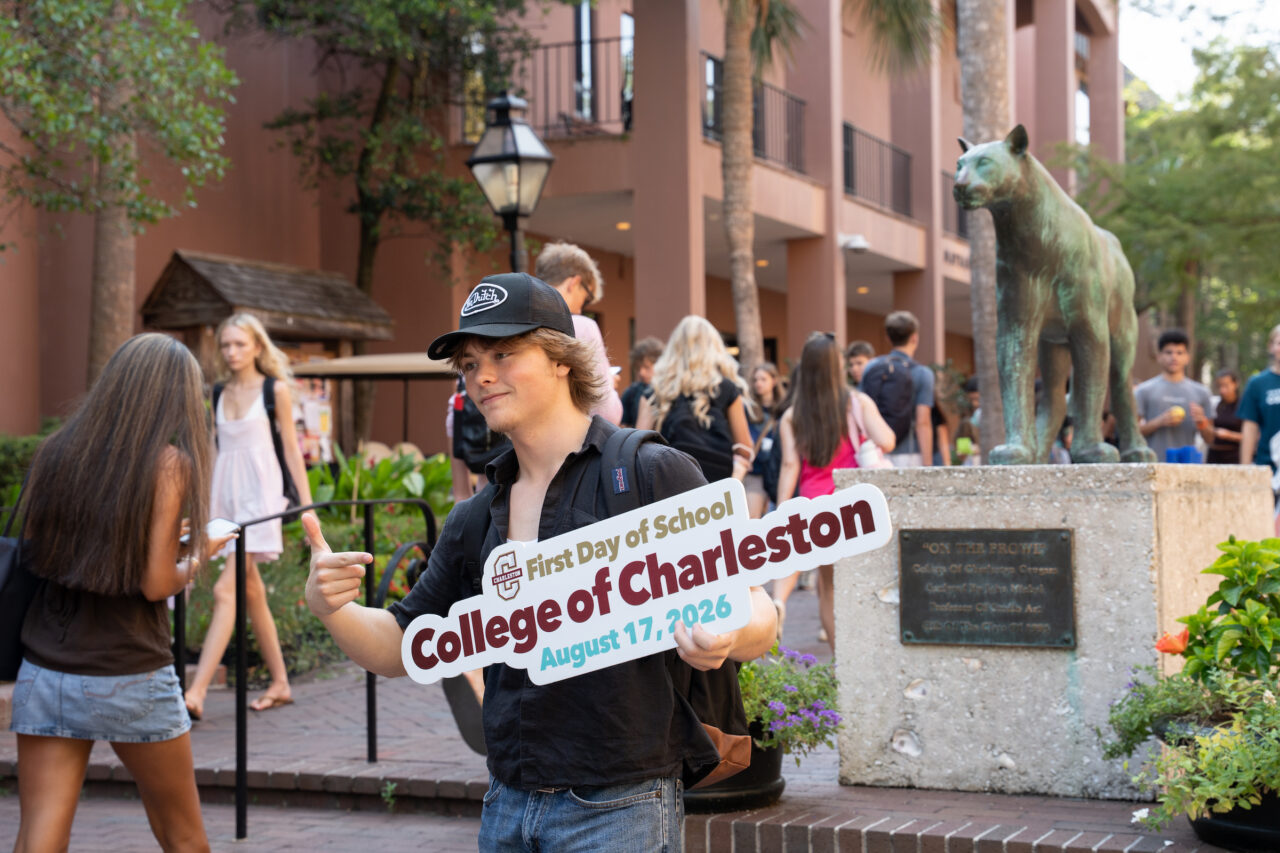 A student holds a sign celebrating the First Day of School at the College of Charleston on August 17, 2026, while standing near a campus statue.