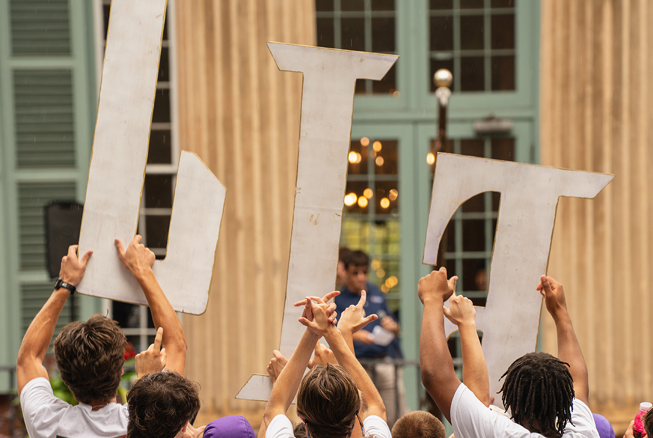 A group of people hold up large white letters spelling "LIT" in a public space.