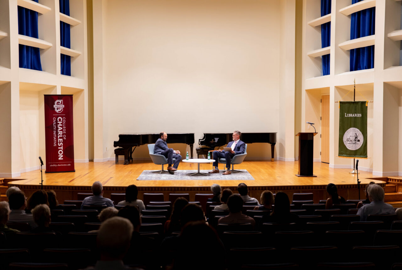 wide shot of theater with two speakers sitting in chairs on stage
