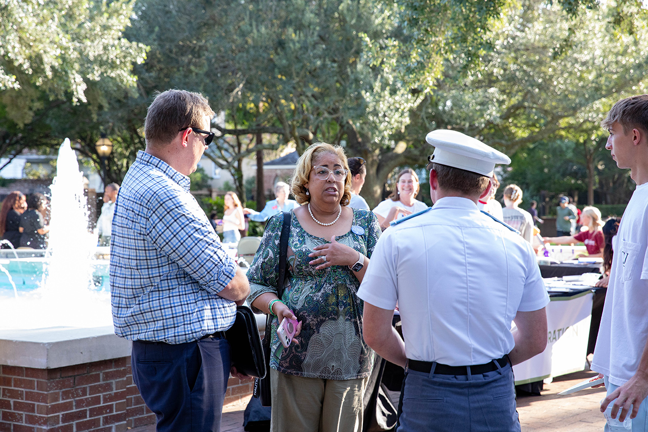 A group of people engage in conversation outdoors near a fountain, with one individual in a white uniform and another holding a phone.