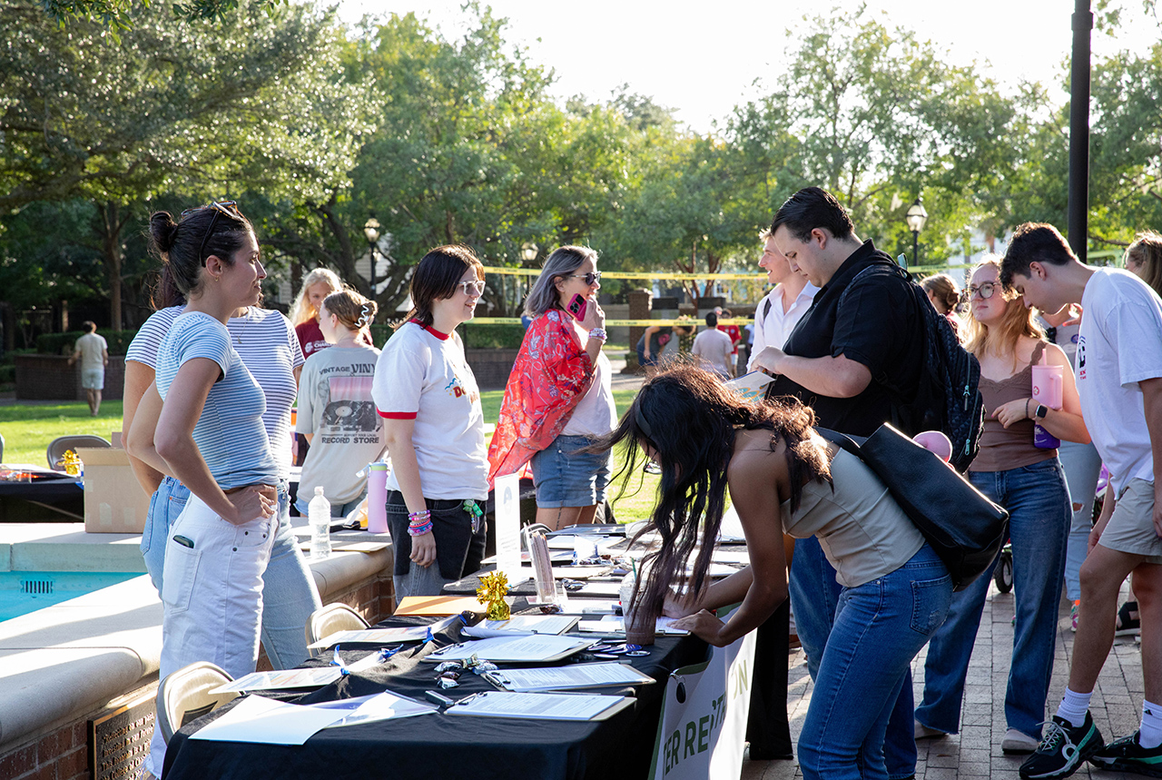 A group of people gather around a table outdoors, where one individual is signing paperwork while others converse and observe.