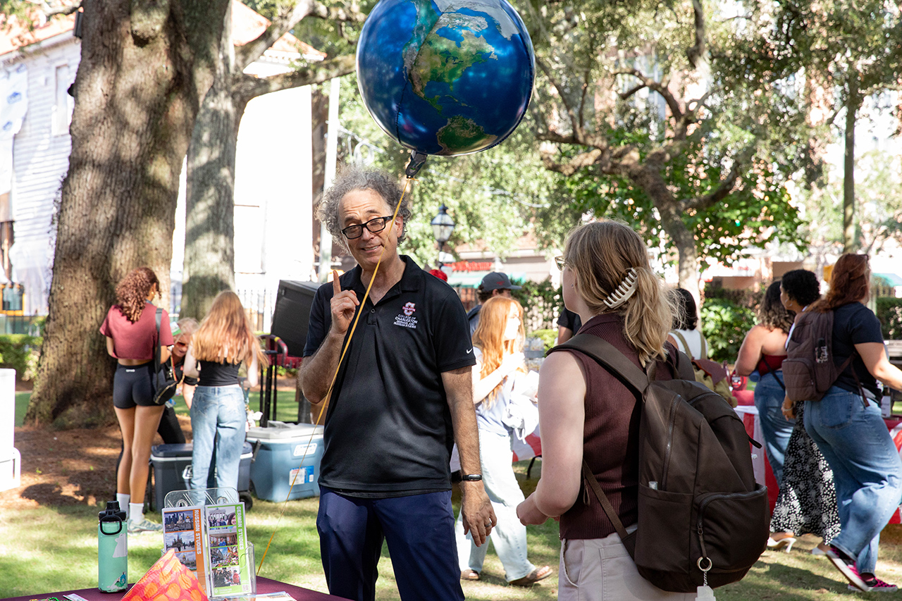 A person holds a large globe balloon while speaking to another individual at an outdoor event.