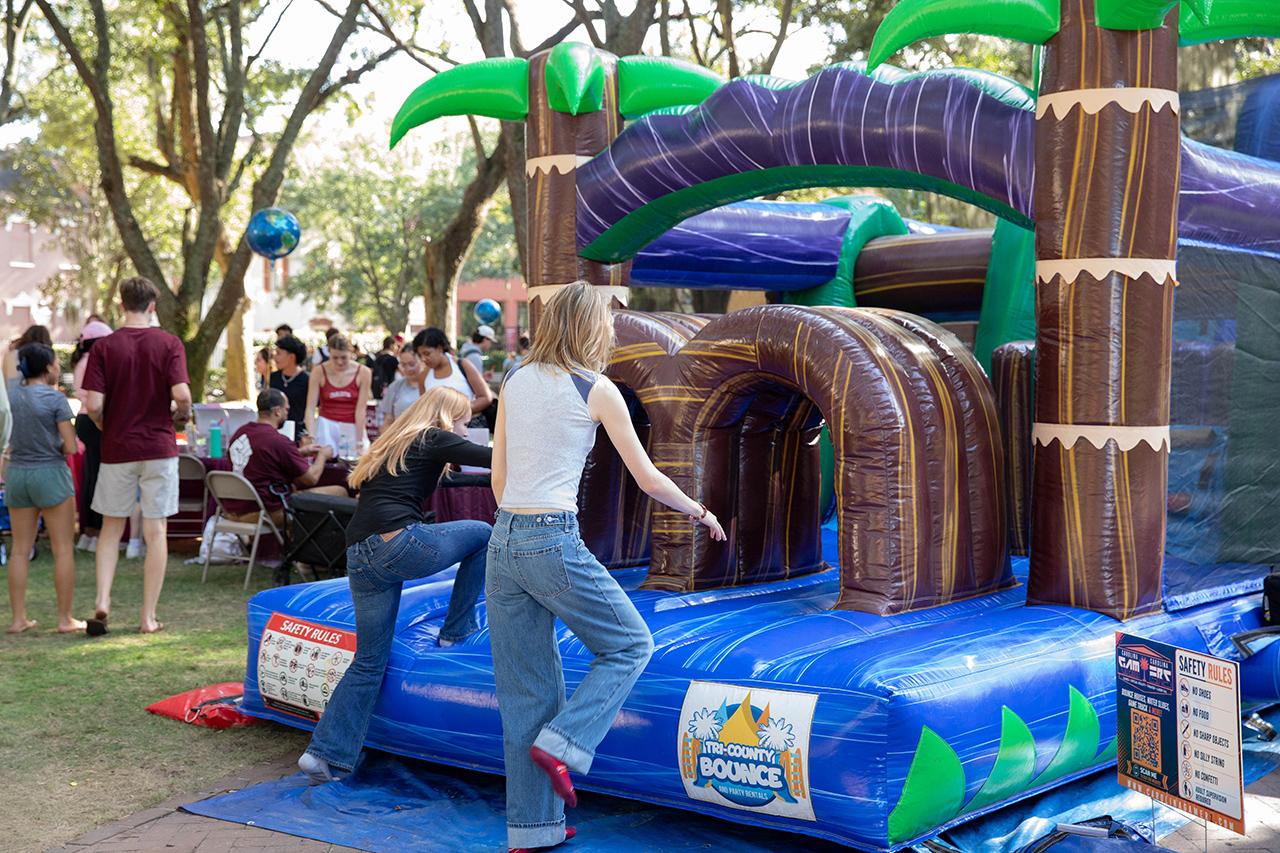 Two individuals approach a large inflatable bounce house with palm tree decorations at an outdoor event.