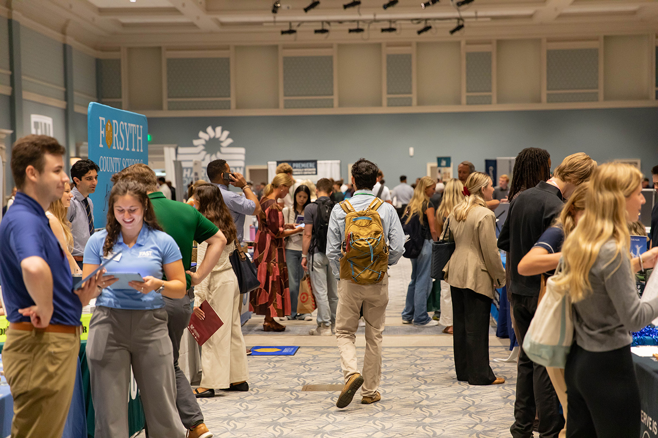 A bustling career fair with attendees engaging with various booths, including one for Forsyth County Schools.