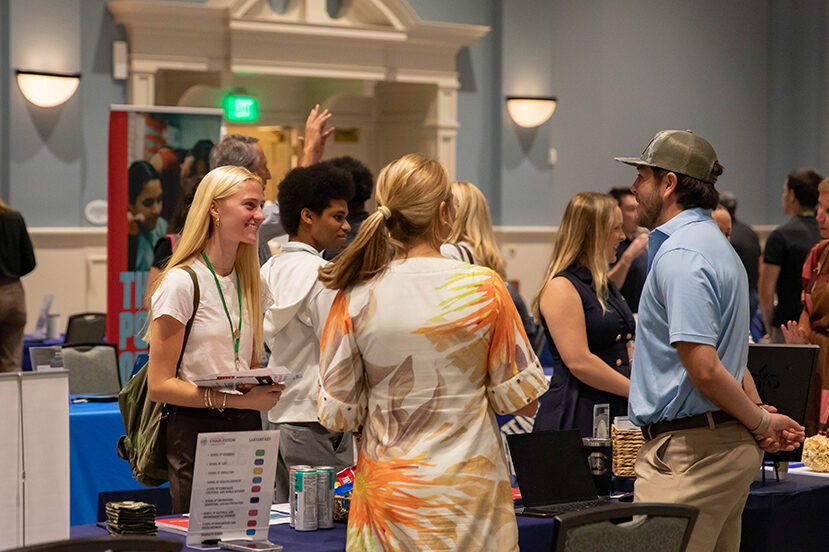 Attendees engage in conversation at a professional networking event with booths and informational displays.