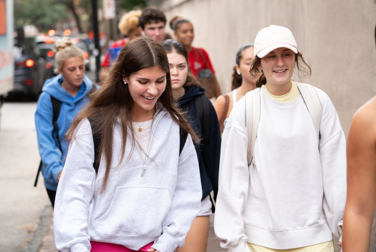 Two young people smile while walking down a city street, surrounded by others in a casual, urban setting.