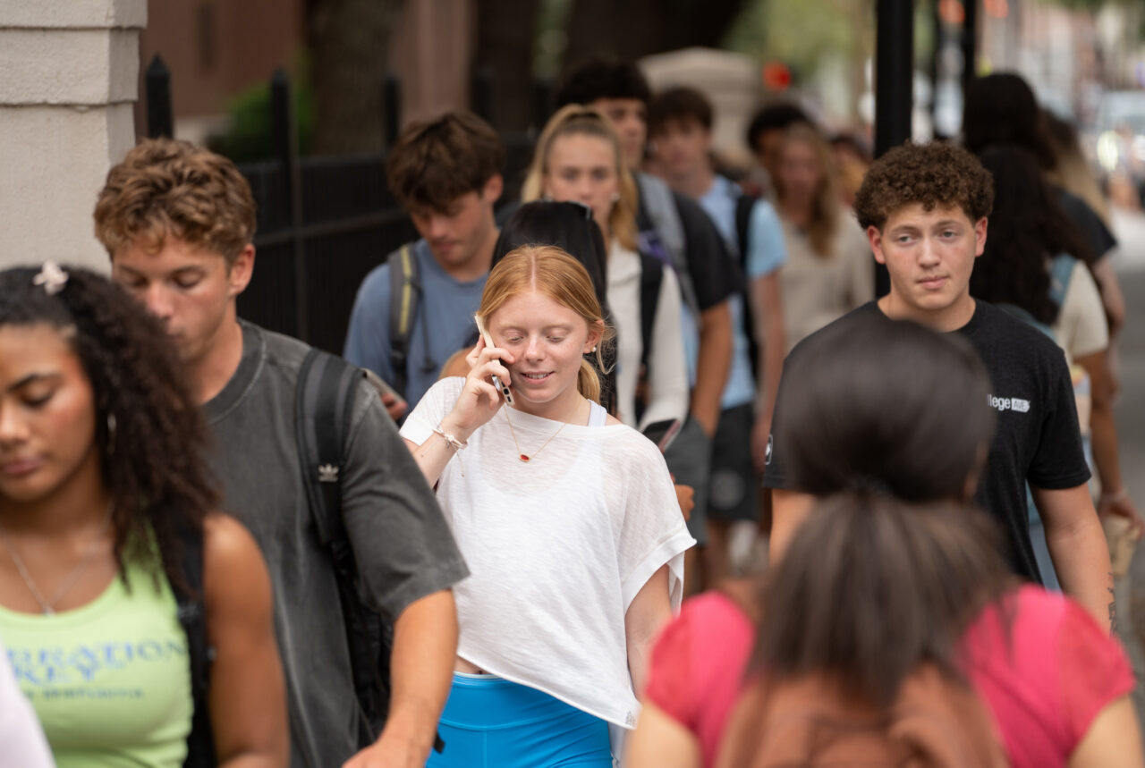 A diverse group of young people walk down a city street, with one person talking on a phone.