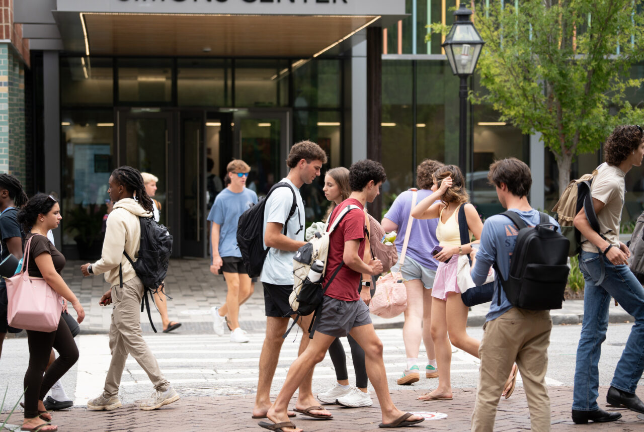 A group of young people walk across a crosswalk in front of a modern building entrance.