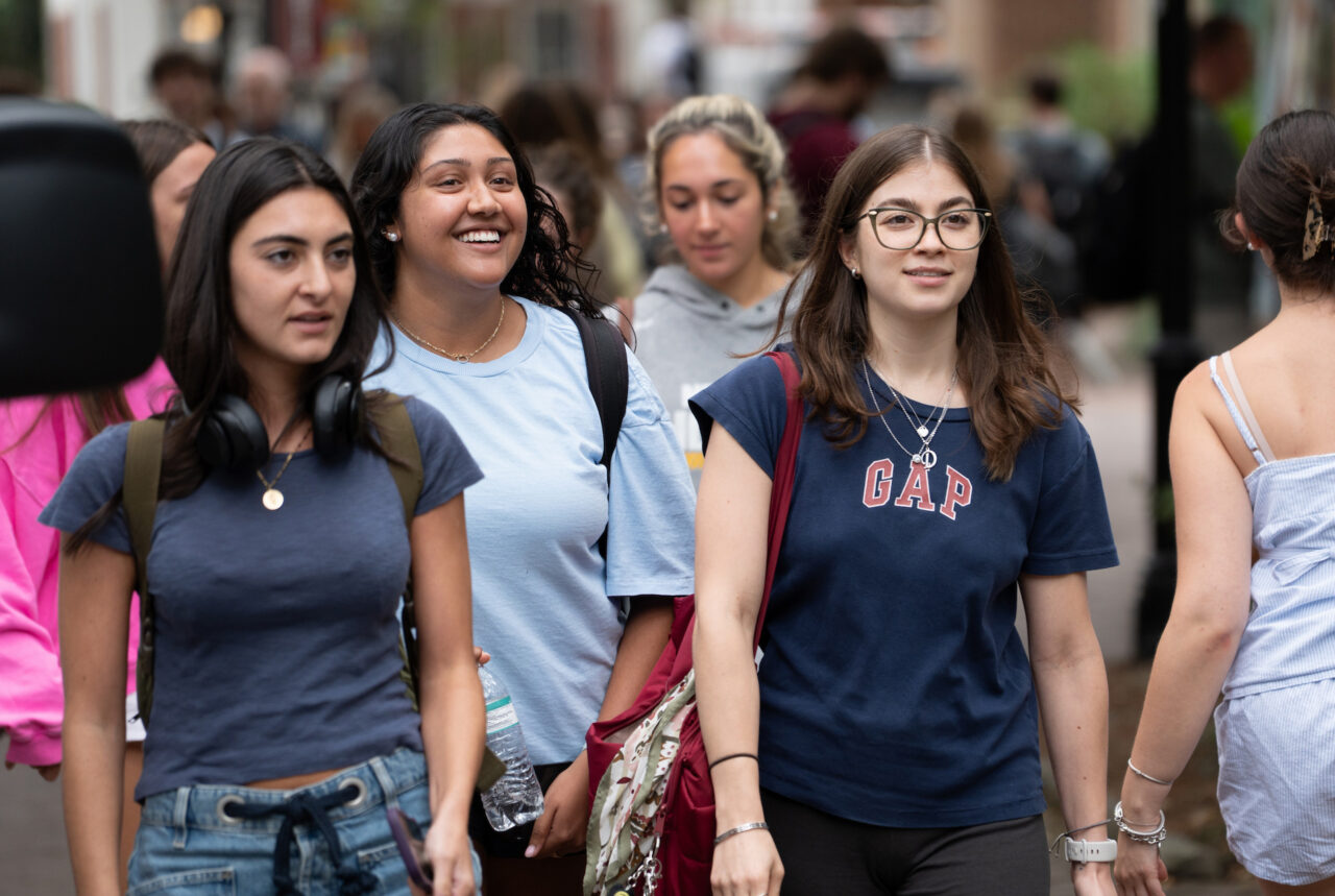 A group of young people walk together down a busy street, some smiling and others looking ahead.