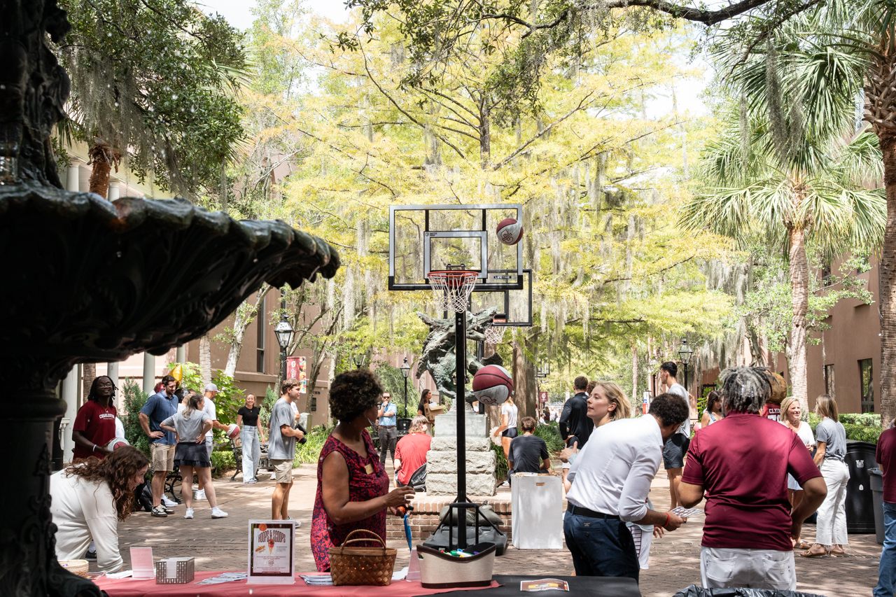 fountain in foreground with people shoot hoops outside in the background