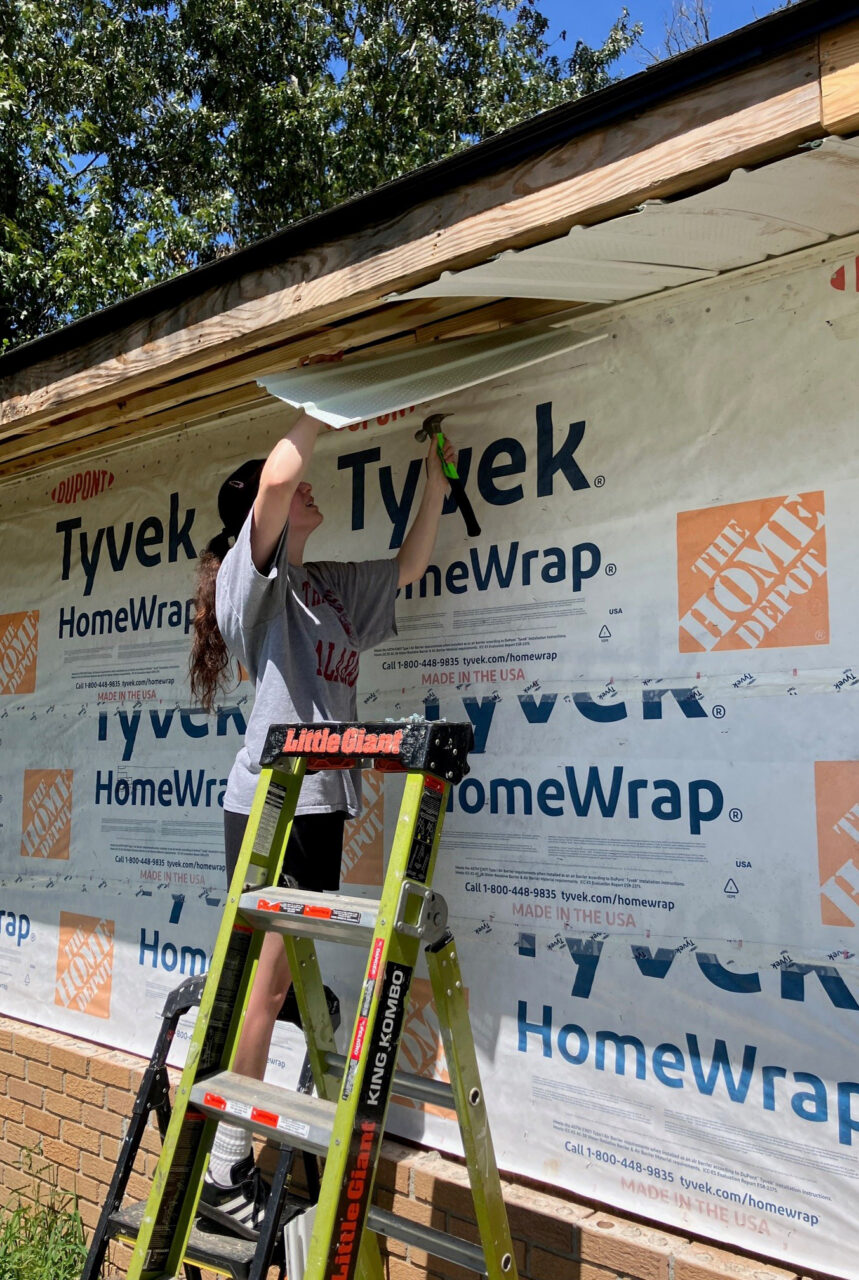 student holds construction material up on roof