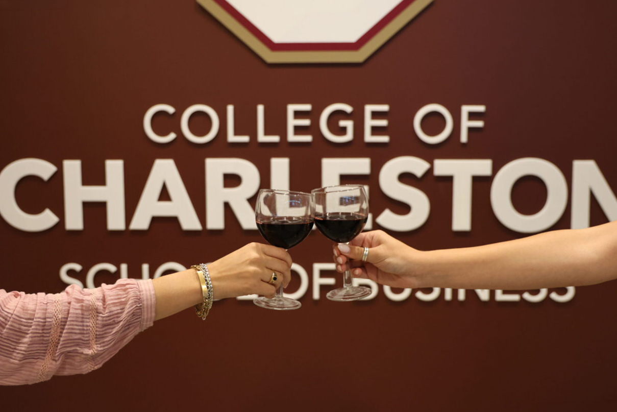 wine glasses clinking in front of College of Charleston School of Business sign