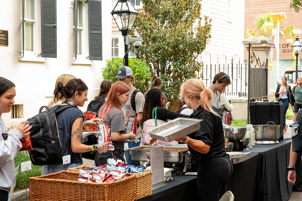 People gather around an outdoor food station, selecting snacks and meals from a vendor.