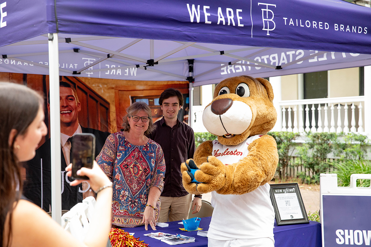 A person in a mascot costume interacts with attendees at an outdoor event under a branded canopy.