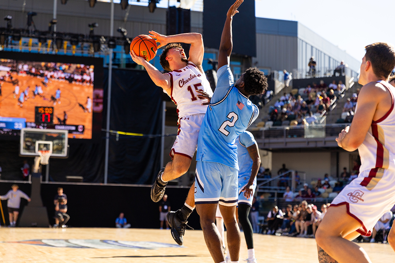 A basketball player in a white jersey with the number 15 leaps to shoot the ball while being defended by an opponent in a blue jersey with the number 2.