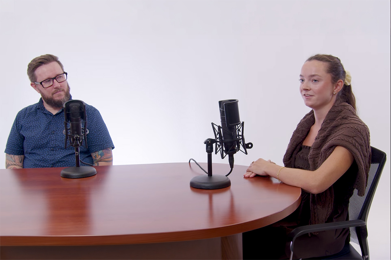 two people sitting at table talking into microphones